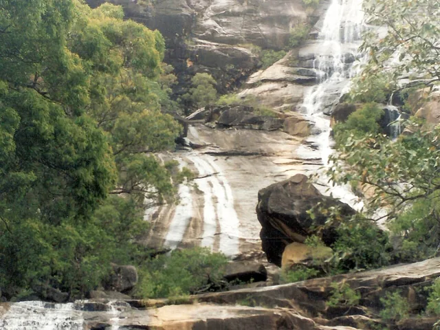 Water runs in white streams down pale granite slabs between forested slopes, with a large boulder in front.