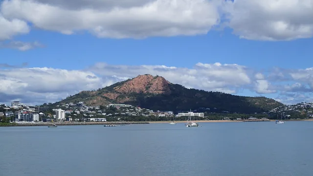 A large pink granite hill rises above waterfront buildings, seen across calm water with a few small boats.