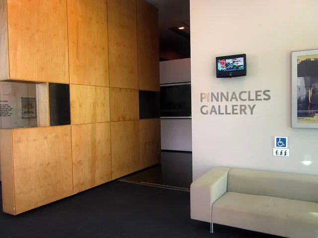 The entrance to an art gallery inside a building, with a wall of pale timber panels and the words Pinnacles Gallery on the wall.